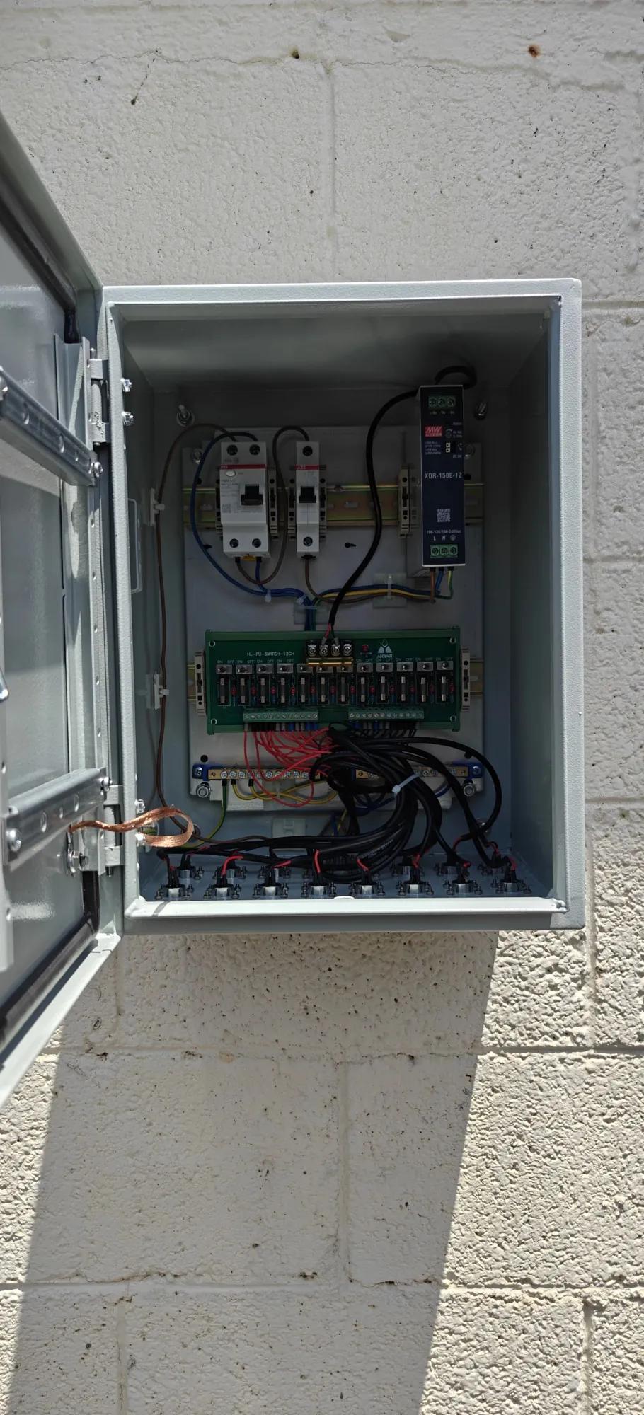 Open wall-mounted power cabinet with protective breakers, a DIN-rail power supply and individually fused output channels feeding glanded cables
