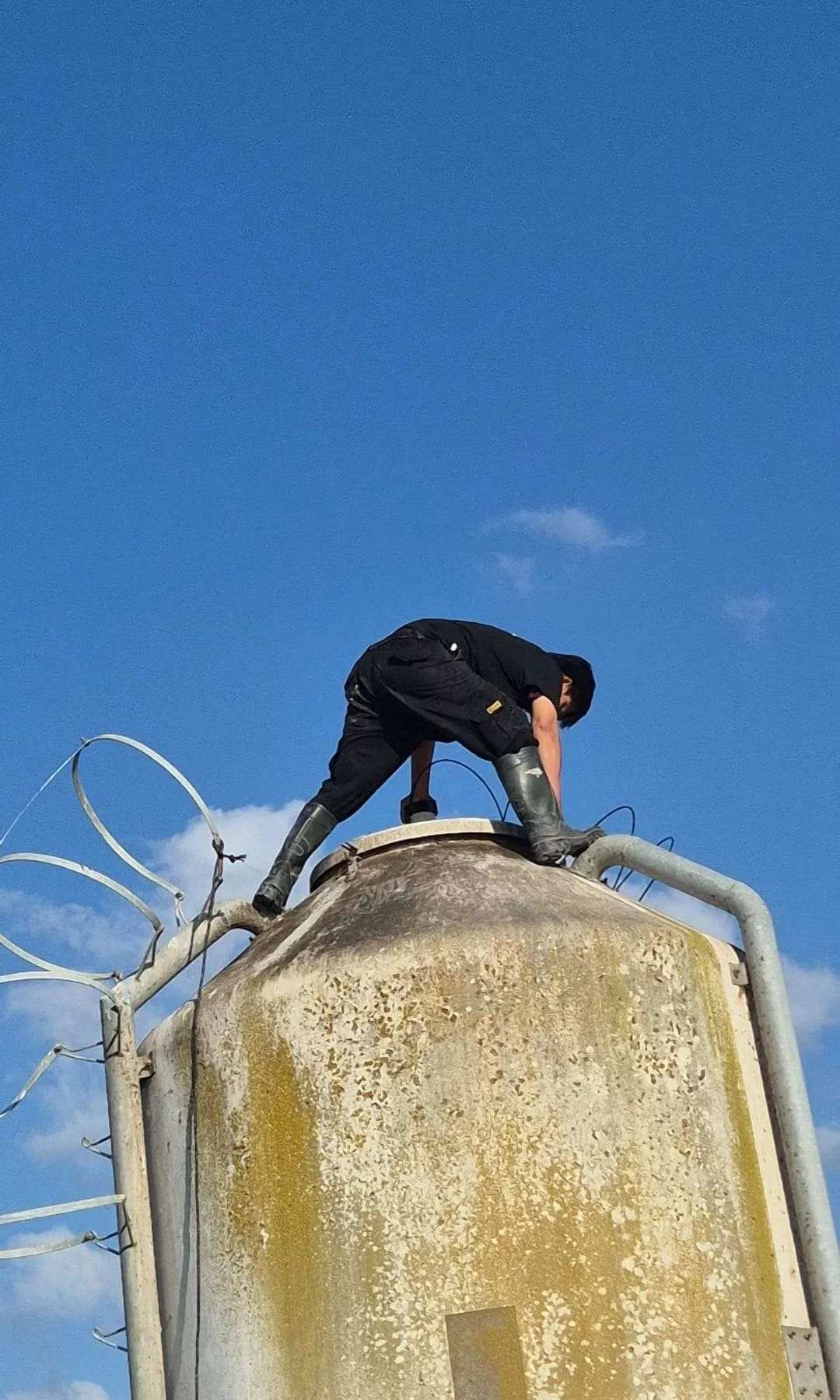 Full height view of the outdoor feed silo from ground level, with a technician at the top working on the hatch